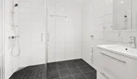 Tomt bad med hvit fliser på vegg og mørke fliser på gulv, dusjhjørne med glassvegger