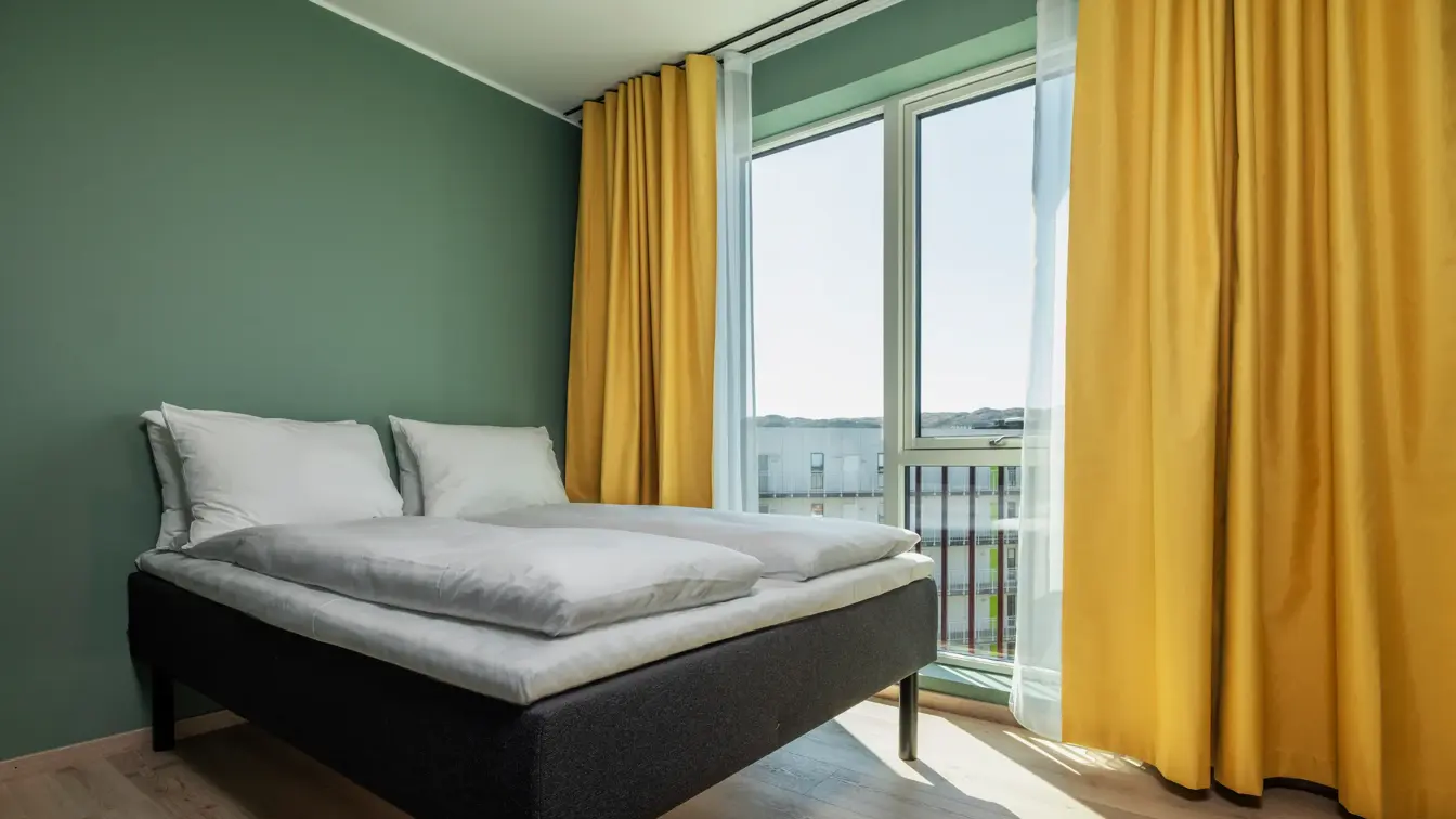 Dobbeltseng i ekstra rom i leilighet. Grønne vegger og gule gardiner
