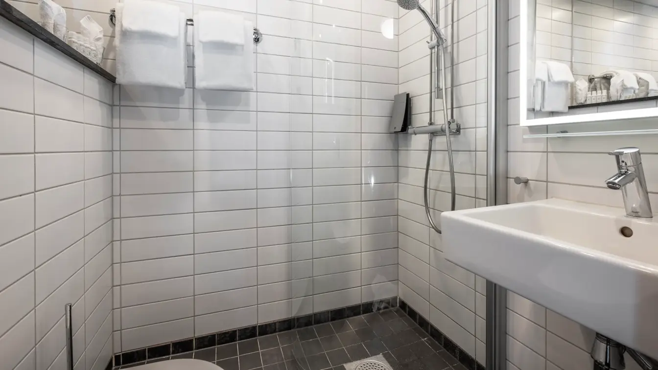 Bad med dusj, håndklær på veggen, servant og speil med lys rundt.