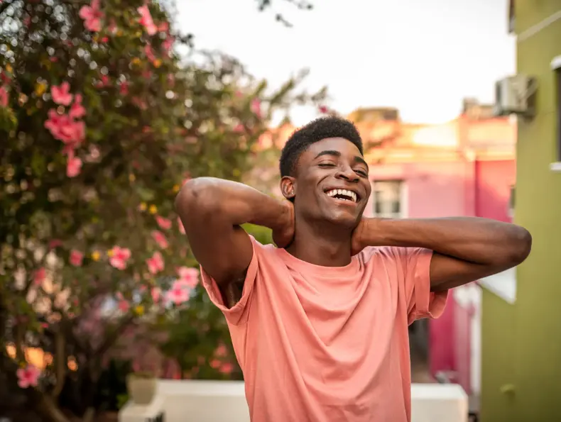 Mann ser mot kamera og smiler med blomster i bakgrunnen 