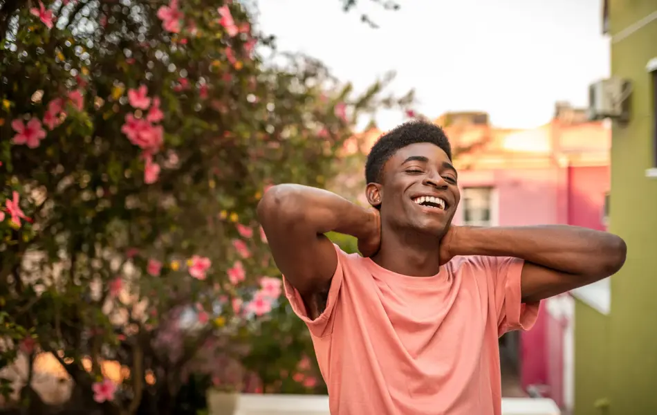 Mann ser mot kamera og smiler med blomster i bakgrunnen 