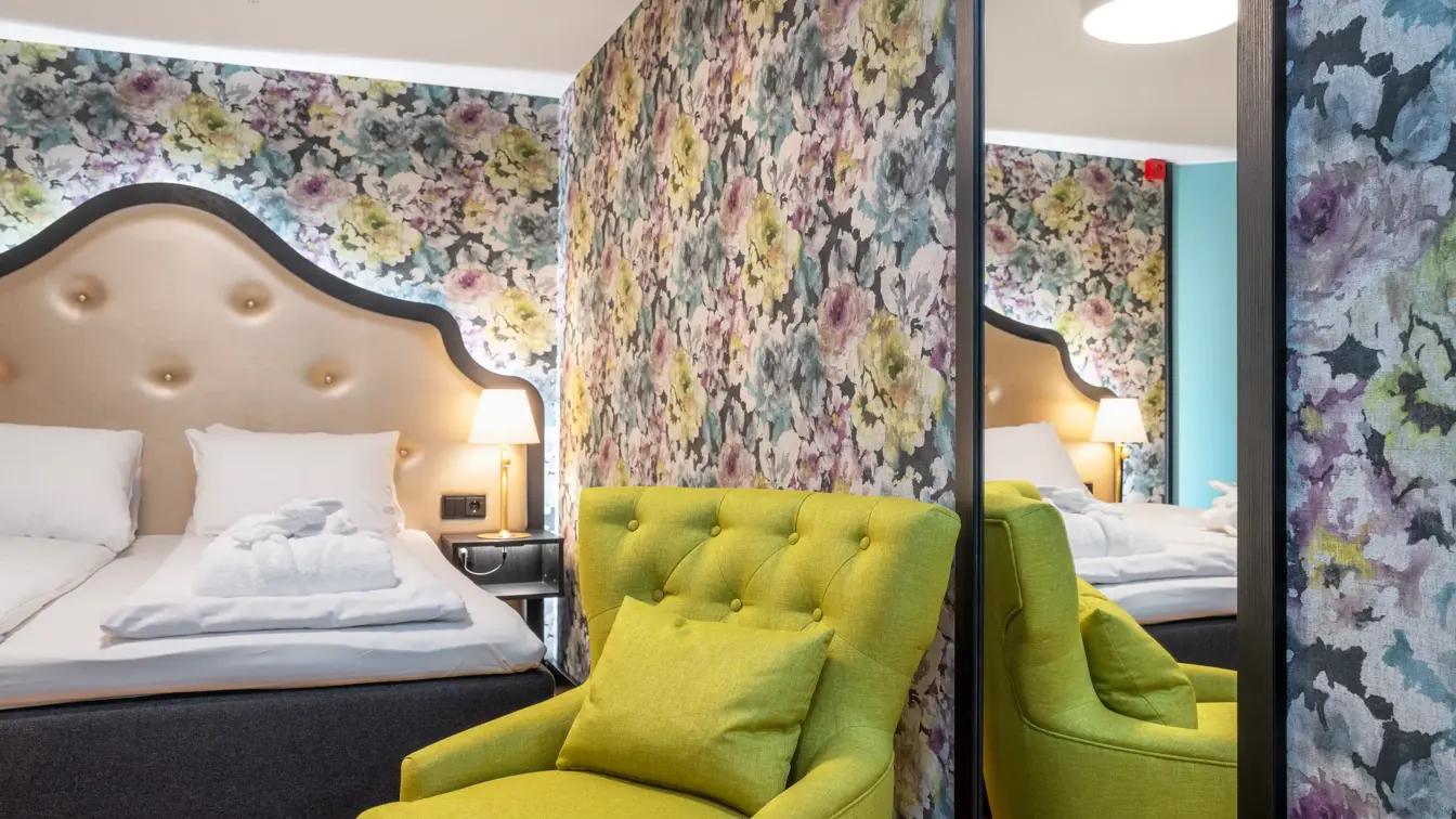 Blomstret tapet og stor dobbeltseng, grønn lenestol og speil i superiorrom på Thon Hotel Cecil i Oslo sentrum