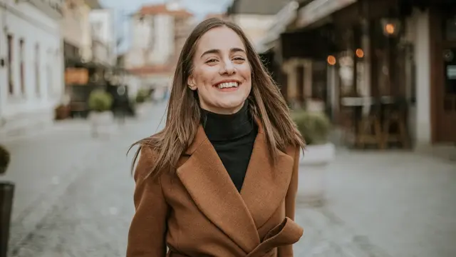 Dame med beige jakke og sort pologenser smiler til kamera