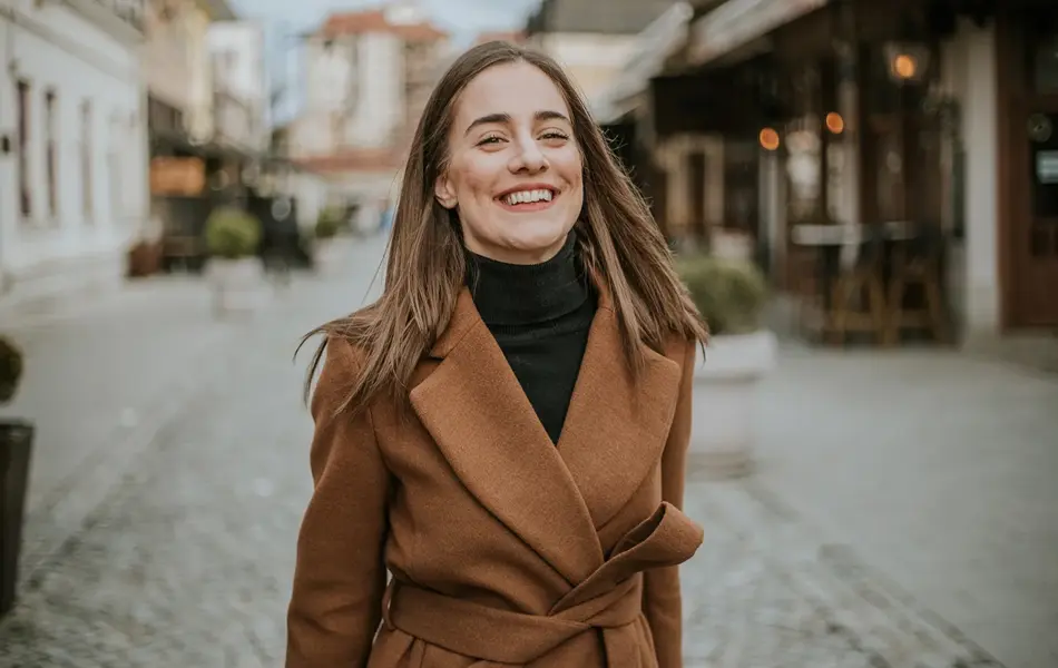 Dame med beige jakke og sort pologenser smiler til kamera