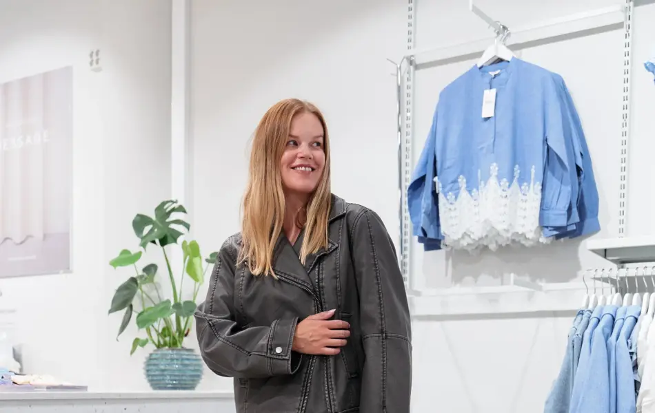 Damemodell i langt grått skjørt, skinnjakke og lyseblå veske.