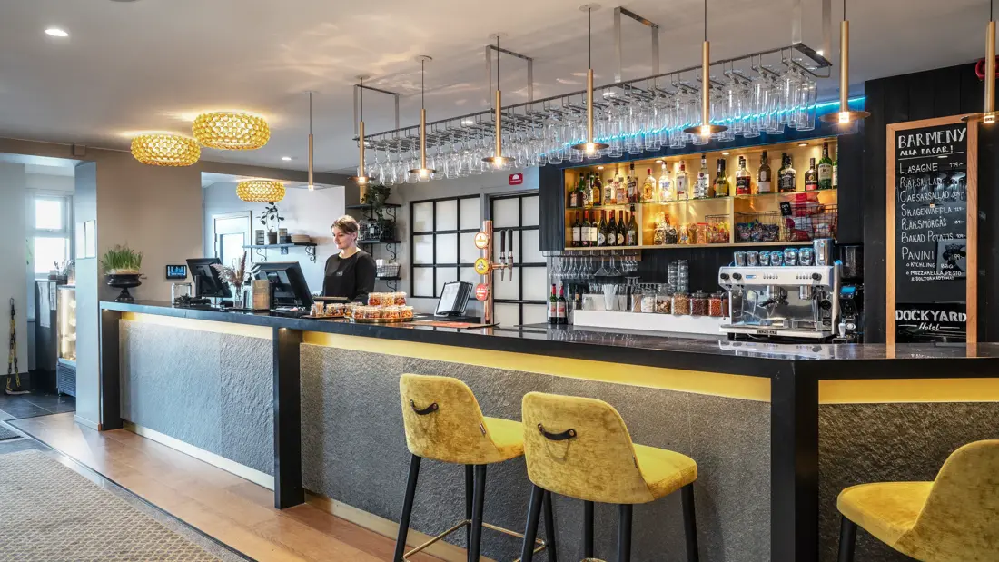 Resepsjonsdisk med lobbybar, resepsjonist bak. disken, gule høye stoler