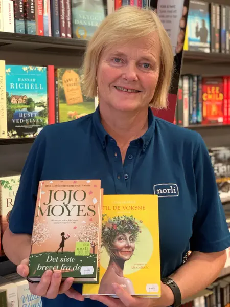 blond norli-ansatt som holder fram to bøker