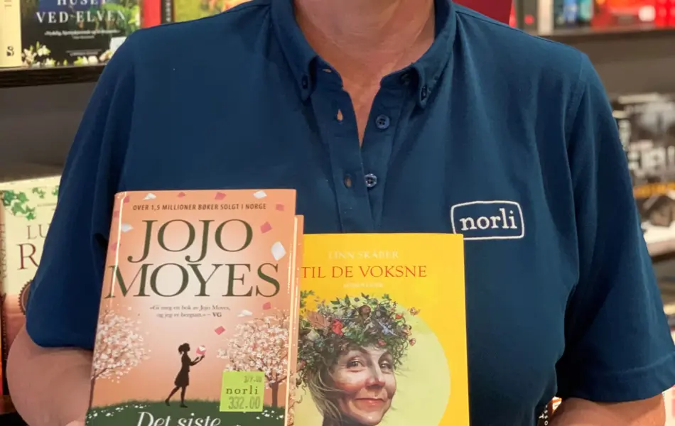 blond norli-ansatt som holder fram to bøker