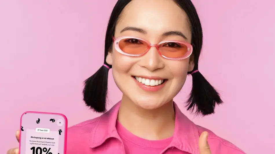 Dame med rosa solbriller og rosa jakke holder mobil med kupongkode