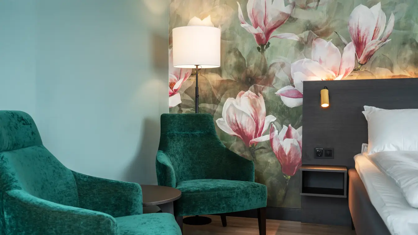 Blomstertapetvegg, salongbord, to grønne lenestoler, salongbord, dobbeltseng, 