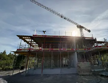 Bildet er fra byggeplassen til boligprosjektet Heggedal Hage i Asker og viser et byggverk med 2 etasjer og en heisekran. Bildet er redigert med KI.