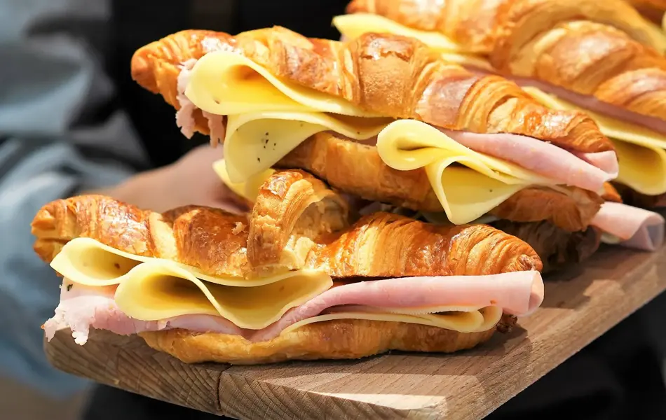 Ansatt som holder trefjøl med croissanter med ost og skinke