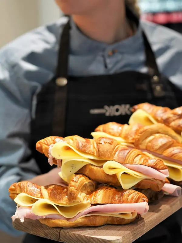 Ansatt som holder trefjøl med croissanter med ost og skinke