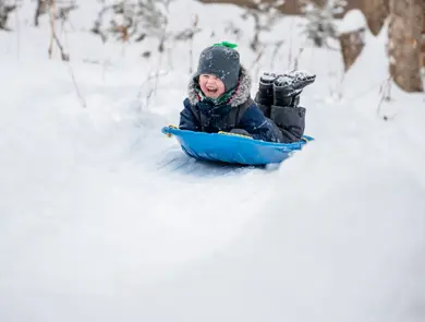 Little Boy Sliding in the Snow Outdoors in Winter. He is smiling and having a lot of fun.