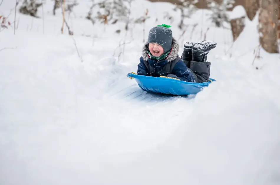 Little Boy Sliding in the Snow Outdoors in Winter. He is smiling and having a lot of fun.