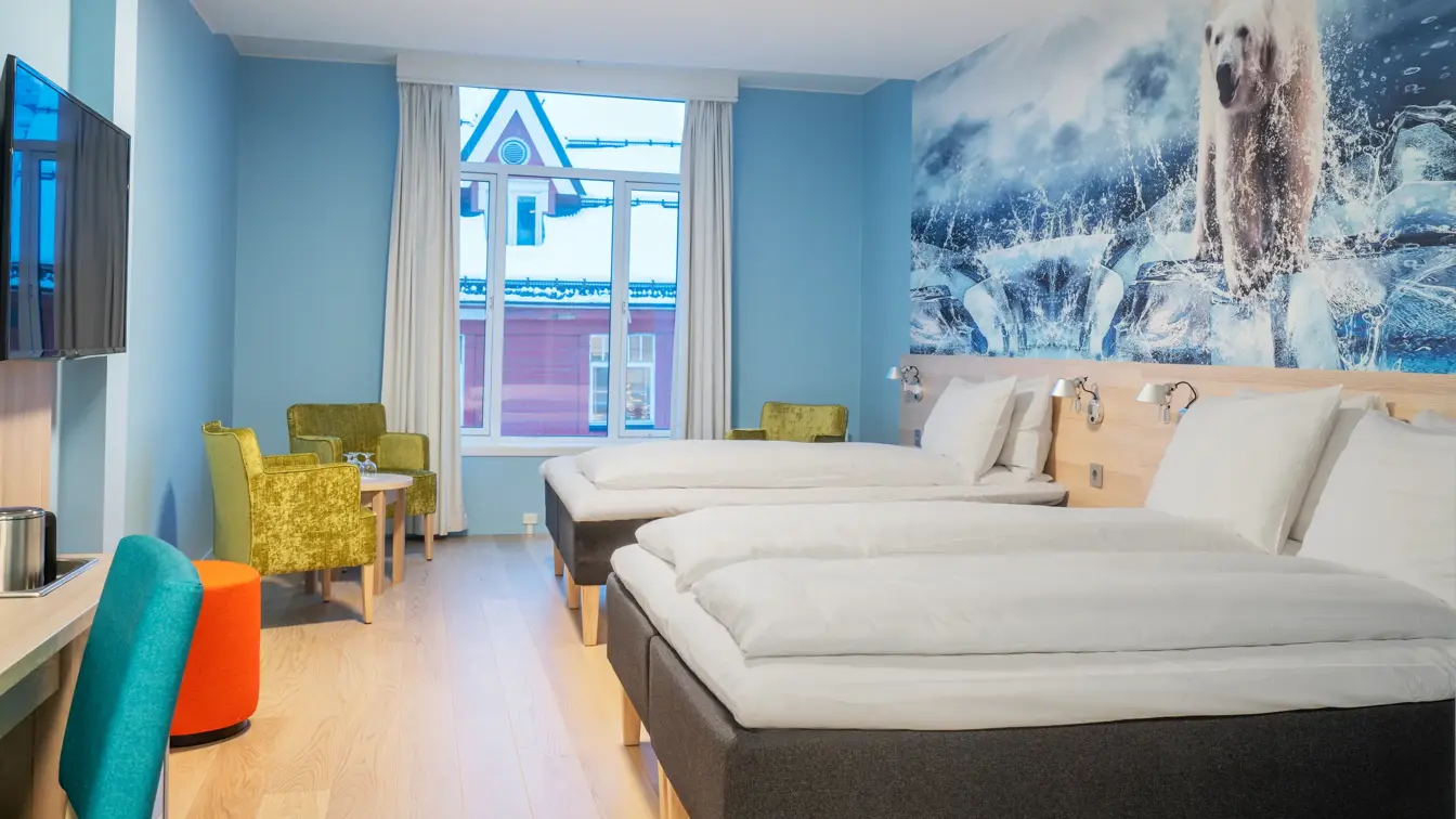Tapetbilde med isbjørn på veggen over sengene, turkise vegger, vindu. Dobbeltseng og enkeltseng, sittegruppe med gule stoler og bord, TV og skrivebord med stol i familierom på Thon Hotel Polar i Tromsø.