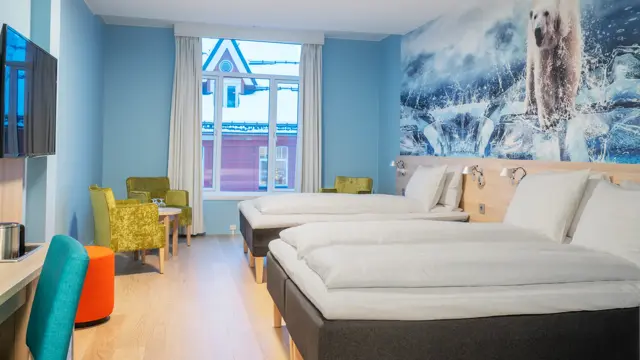 Tapetbilde med isbjørn på veggen over sengene, turkise vegger, vindu. Dobbeltseng og enkeltseng, sittegruppe med gule stoler og bord, TV og skrivebord med stol i familierom på Thon Hotel Polar i Tromsø.