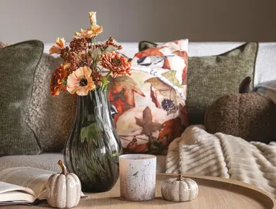 Bord med vase med blomster og sofa med pynteputer i bakgrunn