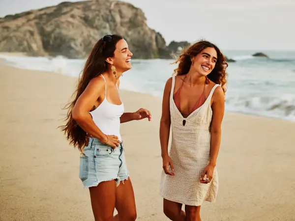 Medium wide shot of laughing female friends hanging out on tropical beach at sunset while on vacation