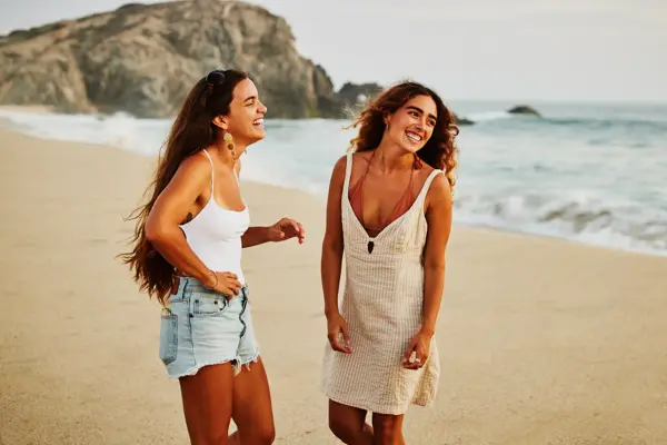 Medium wide shot of laughing female friends hanging out on tropical beach at sunset while on vacation