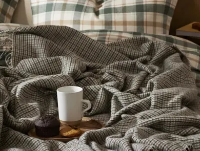 En muffin og kaffekopp står oppe på et lite brett som står på en sneg med et ullpledd over.