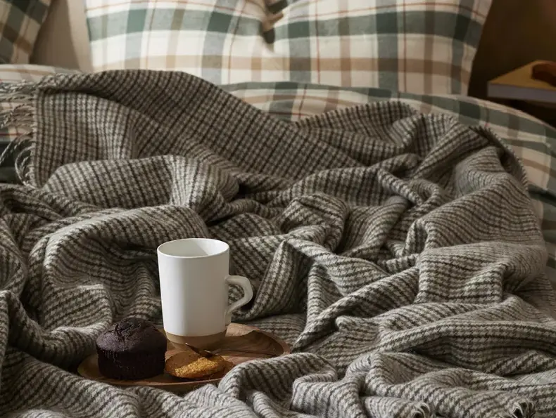 En muffin og kaffekopp står oppe på et lite brett som står på en sneg med et ullpledd over.