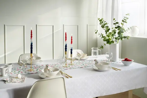 Langbord dekket med hvit duk, løper med blomster, vase med blomster, hvitt service og lysestaker.