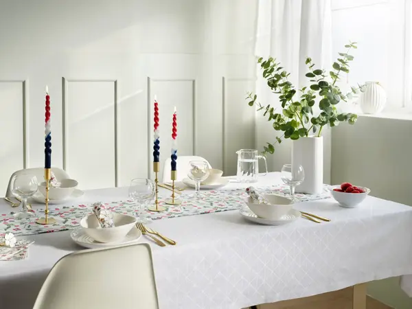 Langbord dekket med hvit duk, løper med blomster, vase med blomster, hvitt service og lysestaker.