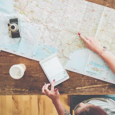 Persom med kart, kaffe, ipad og kamera på et bord som planlegger reise