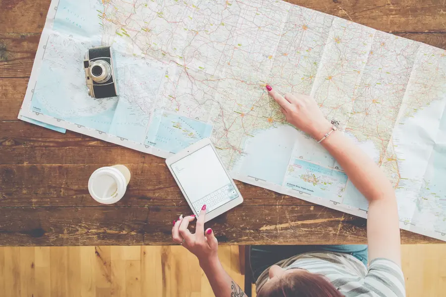 Persom med kart, kaffe, ipad og kamera på et bord som planlegger reise