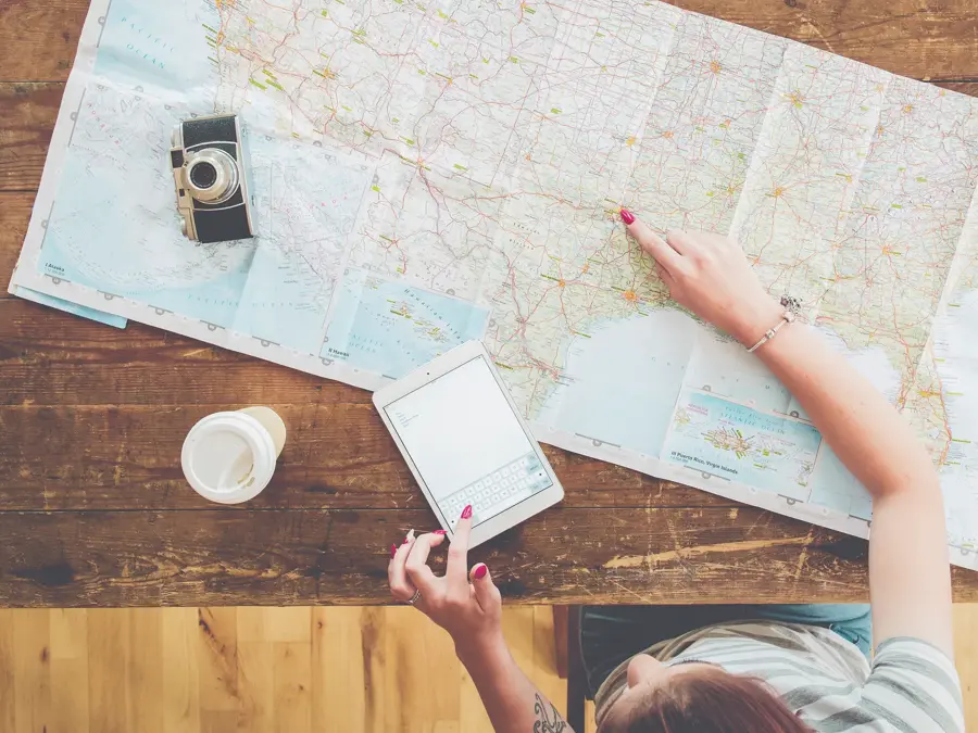 Persom med kart, kaffe, ipad og kamera på et bord som planlegger reise