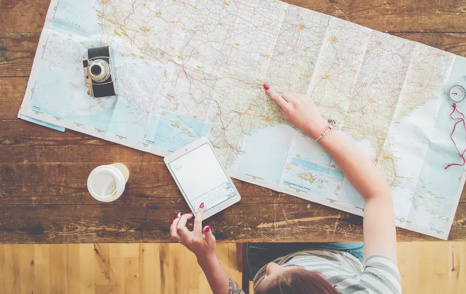 Persom med kart, kaffe, ipad og kamera på et bord som planlegger reise