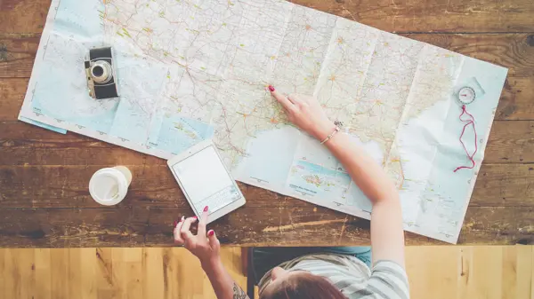 Persom med kart, kaffe, ipad og kamera på et bord som planlegger reise