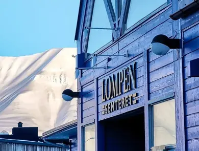 Fasaden til Lompensenteret, skilt med senterets navn og snødekte fjell i bakgrunnen.