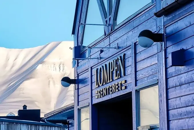 Fasaden til Lompensenteret, skilt med senterets navn og snødekte fjell i bakgrunnen.