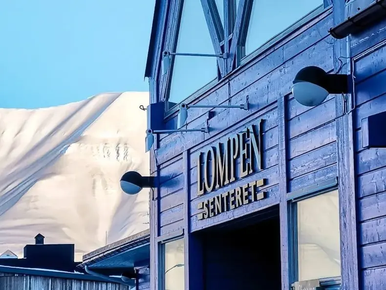 Fasaden til Lompensenteret, skilt med senterets navn og snødekte fjell i bakgrunnen.