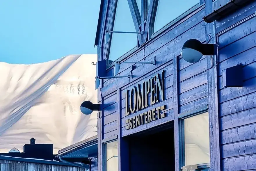 Fasaden til Lompensenteret, skilt med senterets navn og snødekte fjell i bakgrunnen.