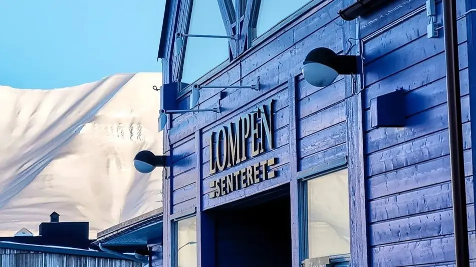 Fasaden til Lompensenteret, skilt med senterets navn og snødekte fjell i bakgrunnen.