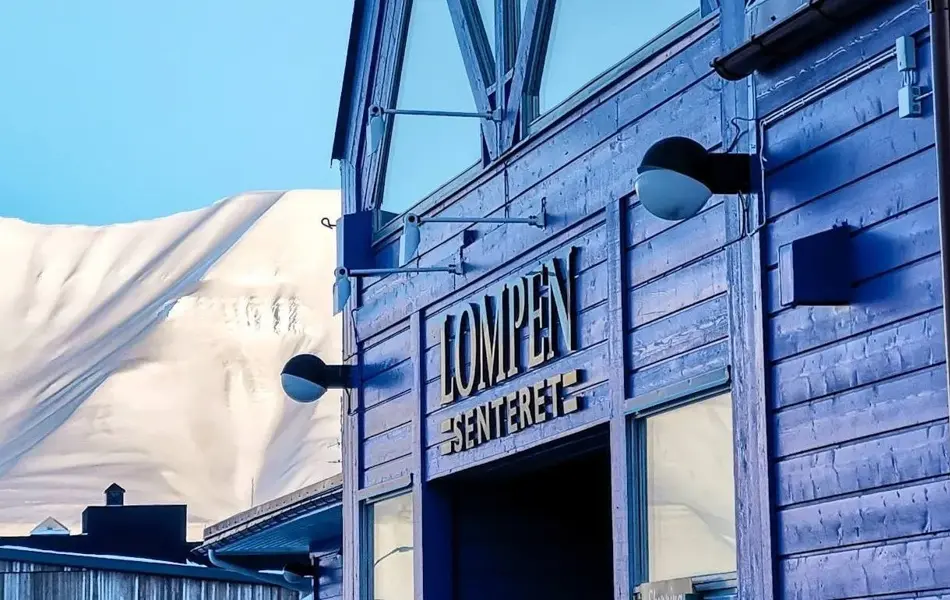 Fasaden til Lompensenteret, skilt med senterets navn og snødekte fjell i bakgrunnen.