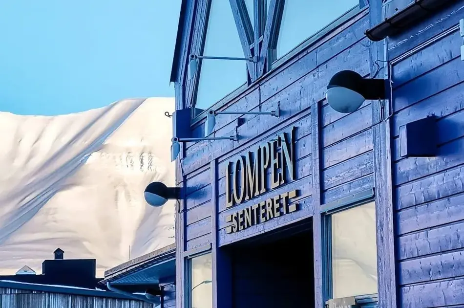 Fasaden til Lompensenteret, skilt med senterets navn og snødekte fjell i bakgrunnen.