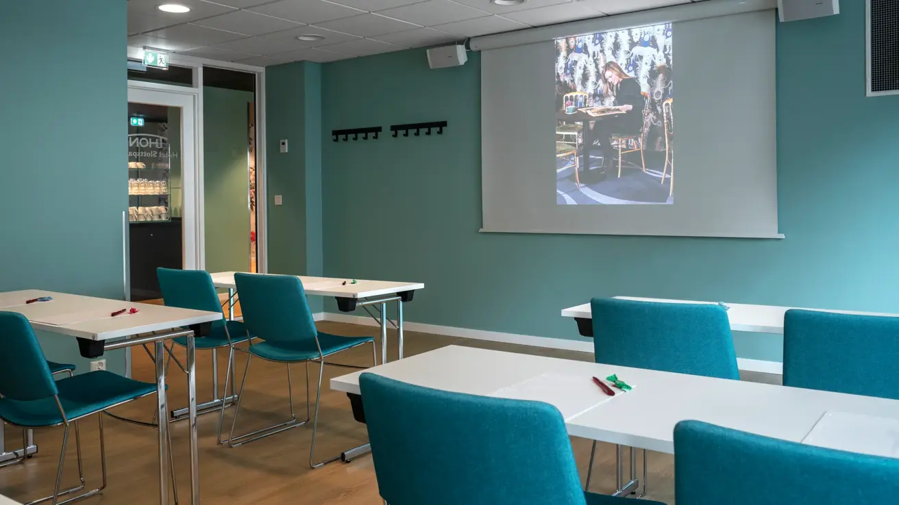 Hvite bord og turkise stoler med turkise vegger i møterom på Thon Hotel Slottsparken i Oslo.