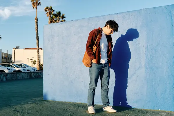 Mann med brun skjorte og skinntotebag poserer inntil blå vegg