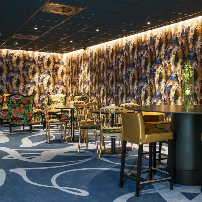 Teppe med mønster og påfugl-tapet, gullfarget barstoler og bord i lounge på Thon Hotel Terminus i Oslo sentrum nær Jernbanetorget
