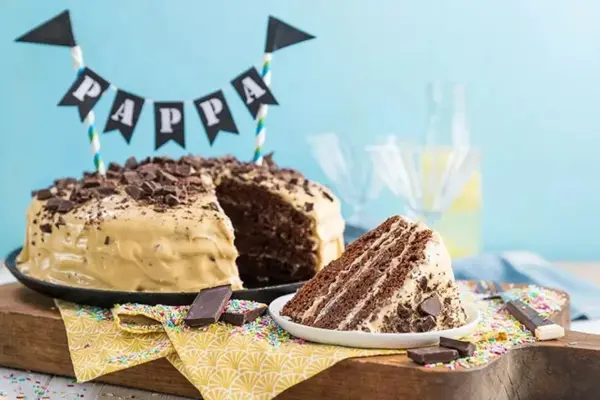 Sjokoladekake med lys krem på et kake fat, en bit er skåret ut og ligger på tallerken.