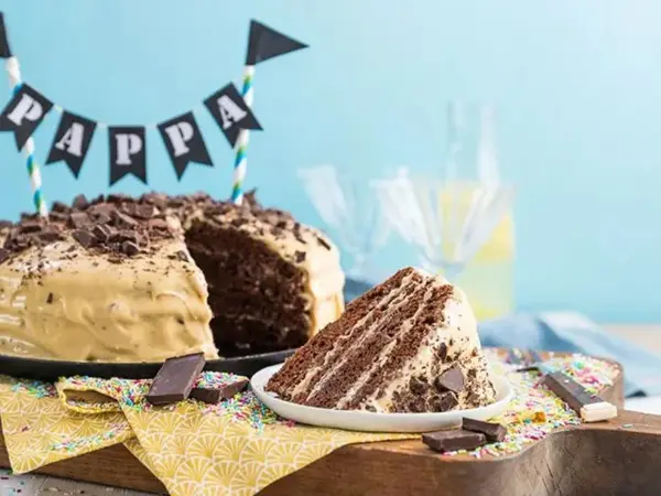 Sjokoladekake med lys krem på et kake fat, en bit er skåret ut og ligger på tallerken.