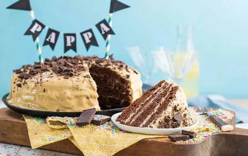 Sjokoladekake med lys krem på et kake fat, en bit er skåret ut og ligger på tallerken.