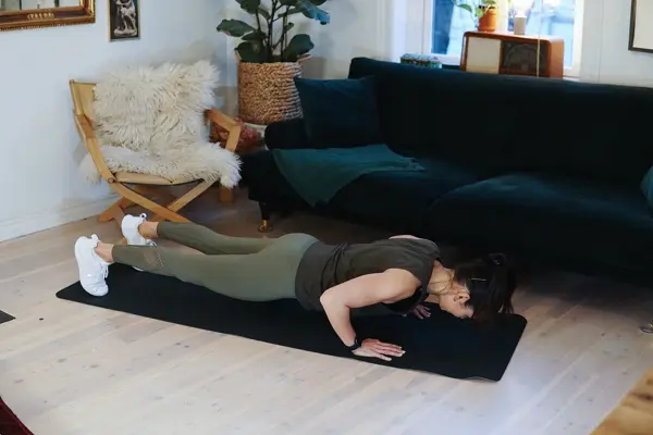 treningsekspert Anna Johansen trener på matte på gulvet, mørkegrønn sofa i bakgrunnen, lys stol med pels oppi, str grønn plante, bilder på veggen