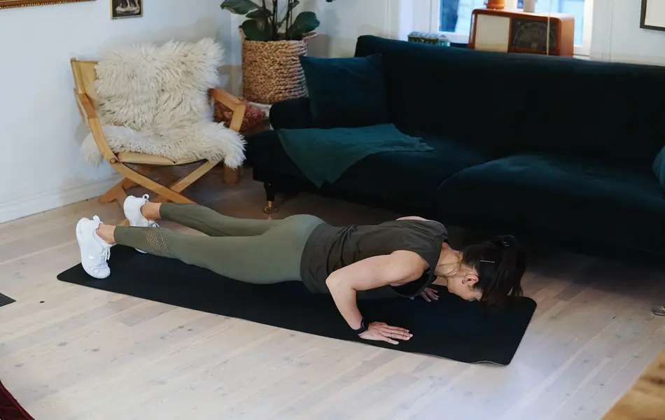 treningsekspert Anna Johansen trener på matte på gulvet, mørkegrønn sofa i bakgrunnen, lys stol med pels oppi, str grønn plante, bilder på veggen