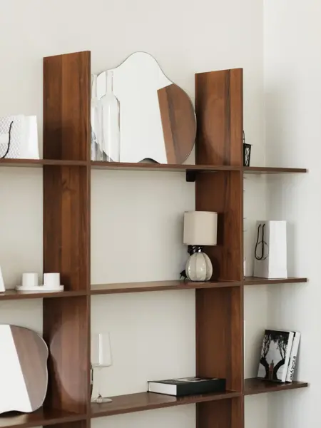 Nærbilde av hylle i mørkt tre med bølgespeil og diverse bøker og  pyntegjenstander 