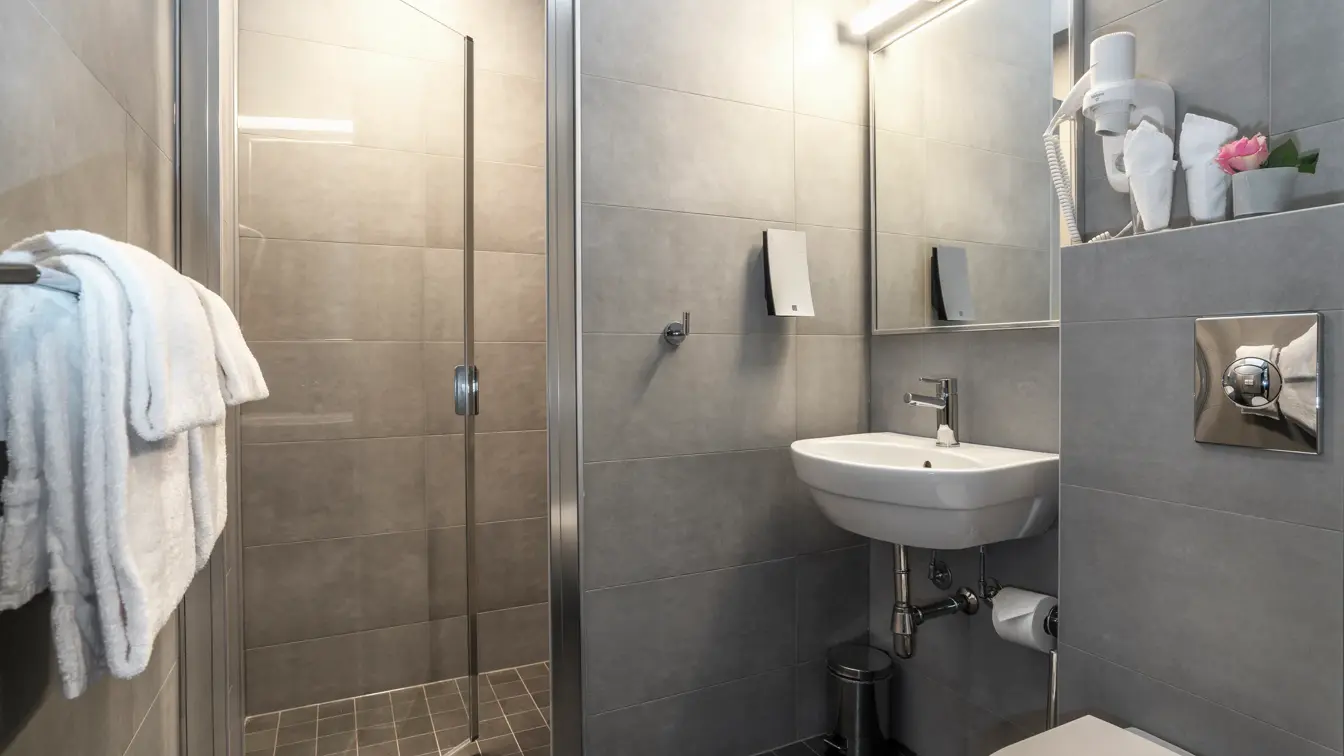 Bad med dusj, grå fliser og servant.